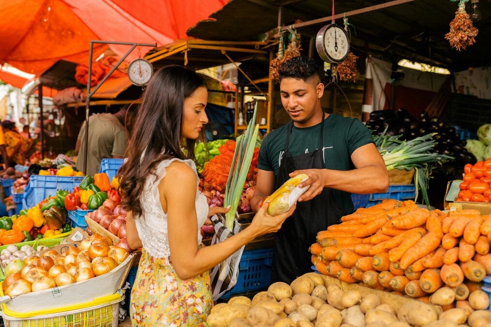 Unsplash market A man shows a woman a vegetable in a market.