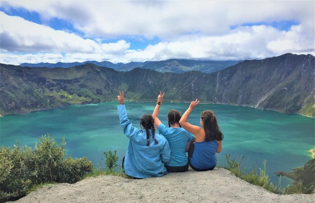 Brooke T., Ecuador Three girls doing peace sign overlooking mountain and lake.