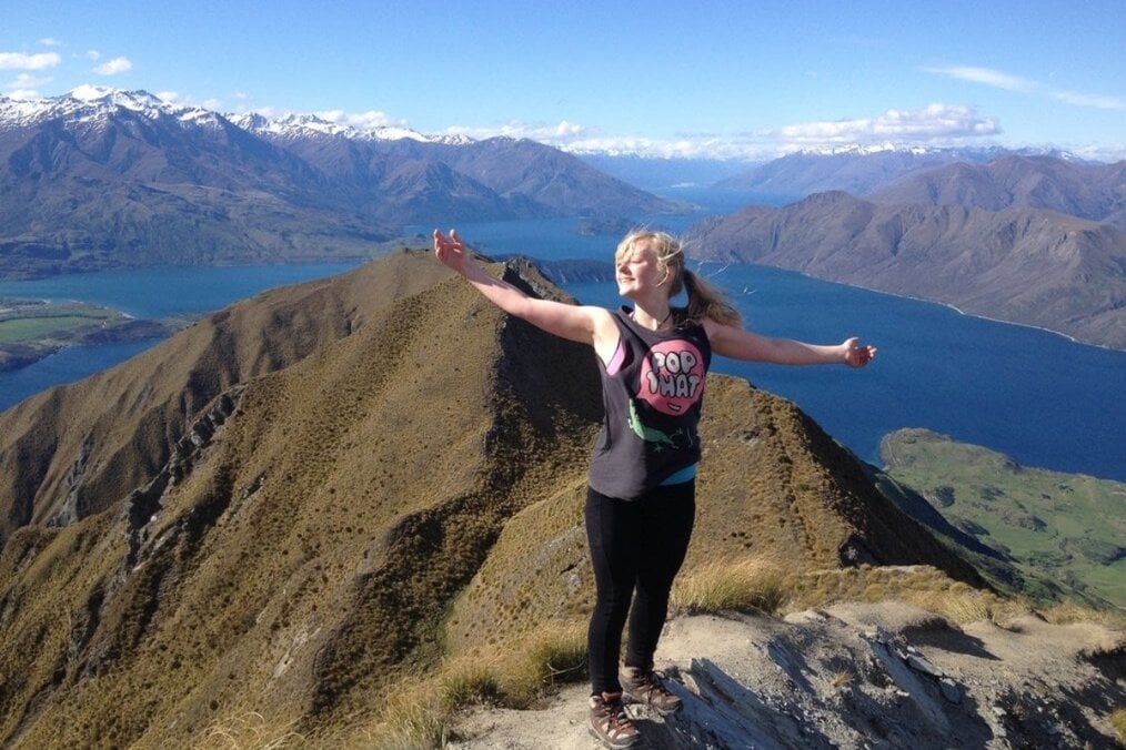 Kaylee P. BCA New Zealand Alum A person standing on top of mountains next to a body of water